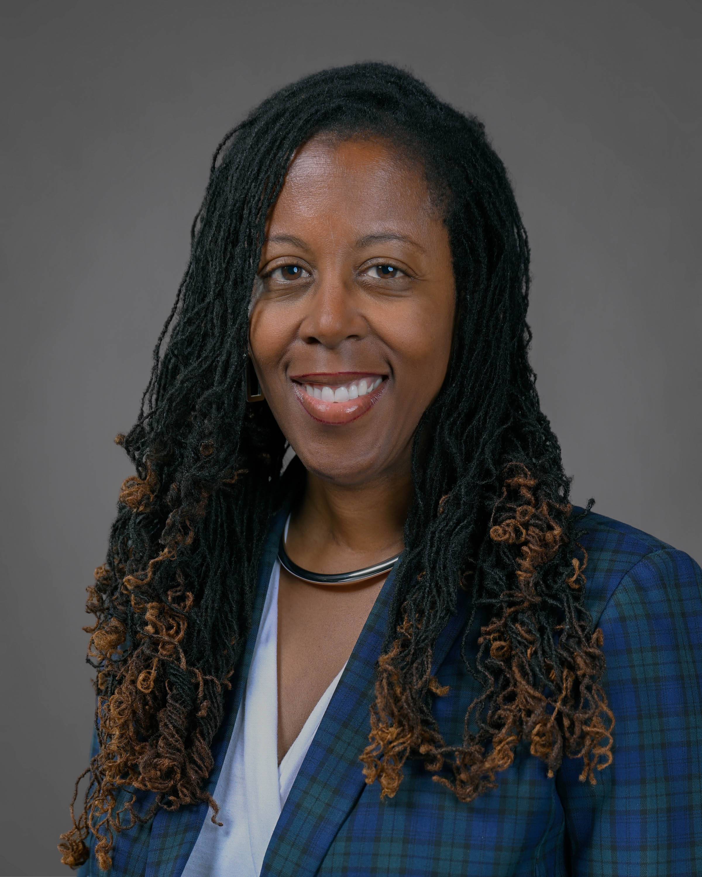 Smiling woman with long curly dark hair in a blue and green plaid jacket